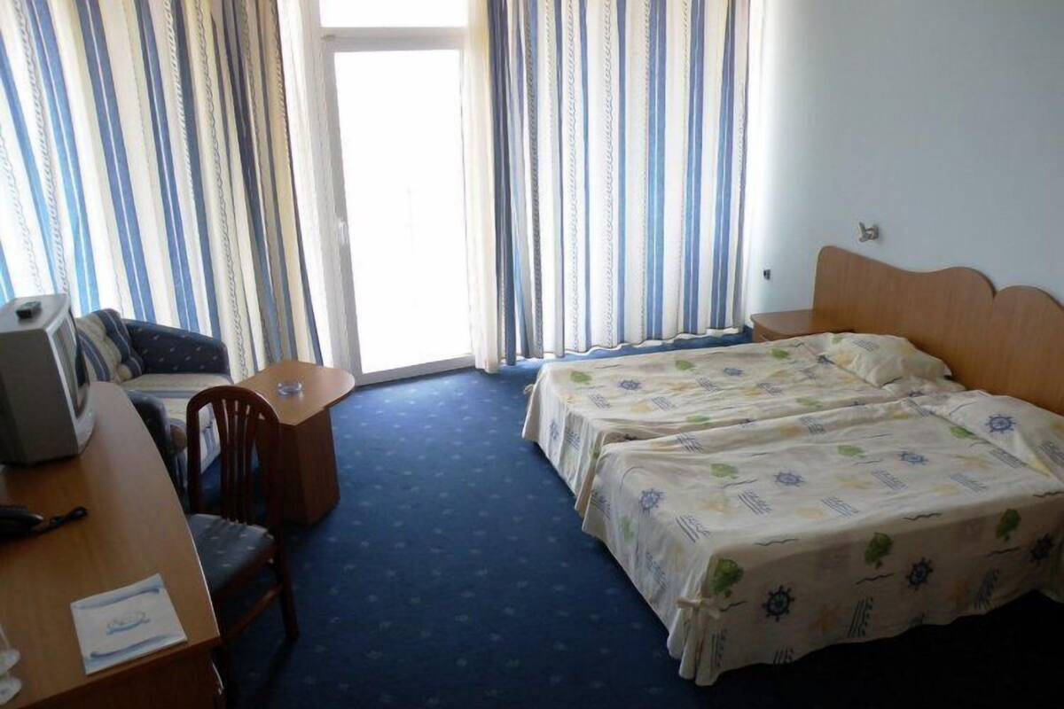 A hotel room with two beds, a desk with a chair, a television, and a window with curtains.