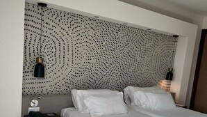 A modern bedroom with a patterned headboard, a bed with white linens, two bedside lamps, and a nightstand with a lamp and a phone. - Hotel Barbato (Naples)