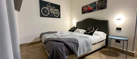 A neatly arranged bedroom with a bed, two wall-mounted lights, a small table, and two artworks on the wall.