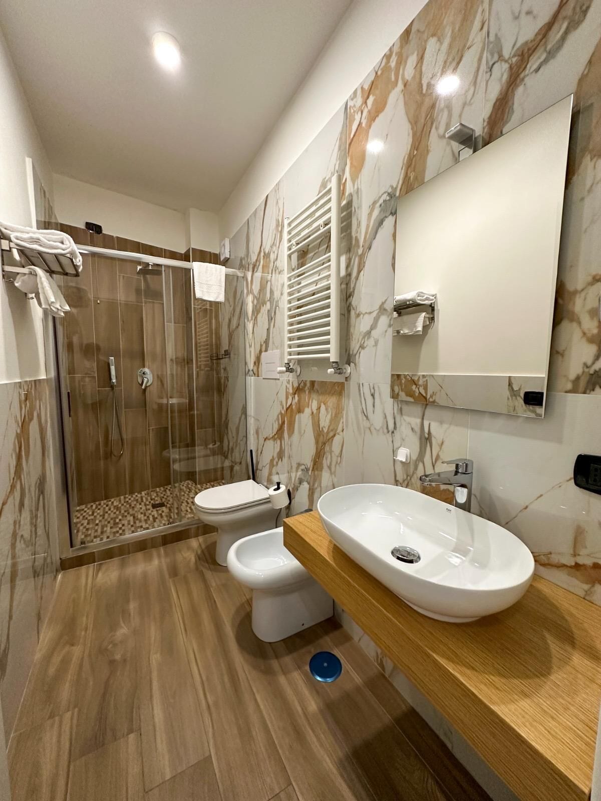 A modern bathroom with a glass-enclosed shower, two toilets, a large sink, and a mirror.
