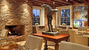 A cozy dining area with a brick fireplace, comfortable seating, and a large window with a view. - Inn at Willow Grove (Orange)