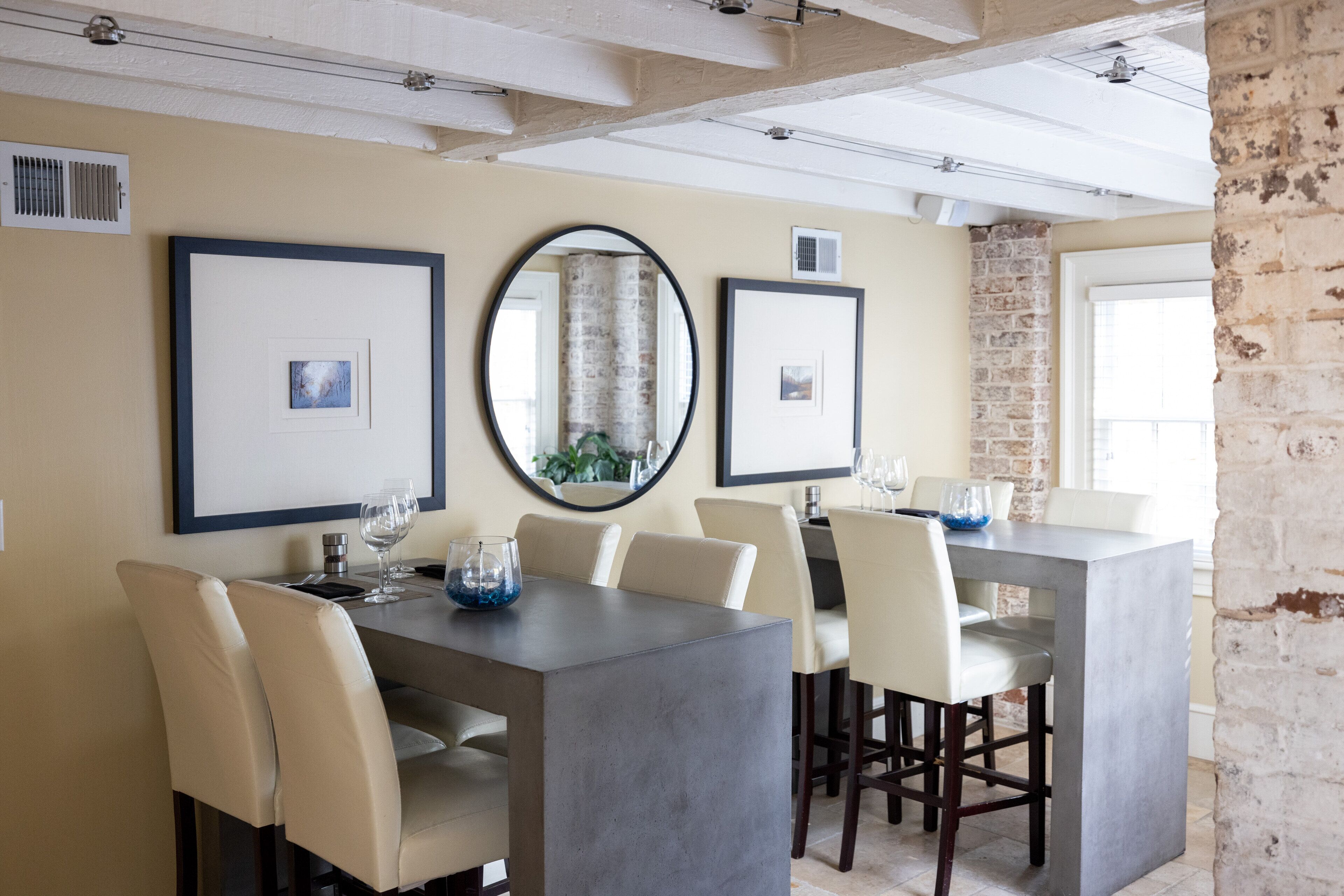 A dining area with a long table, multiple chairs, framed pictures, and a large mirror on the wall.