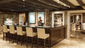 A bar area with a rustic brick wall, wooden ceiling beams, and a bar counter with stools. - Inn at Willow Grove (Orange)
