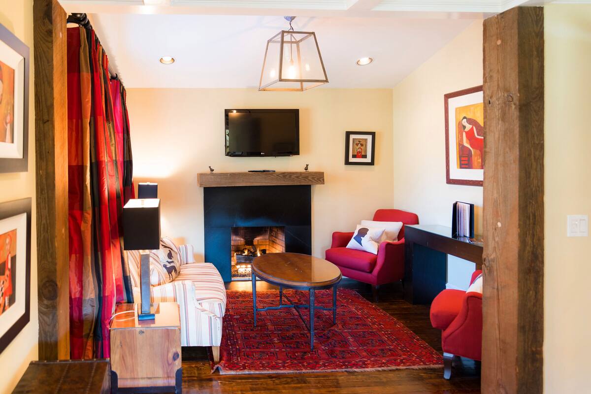 A living room with a fireplace, red chairs, a TV, and a red rug.