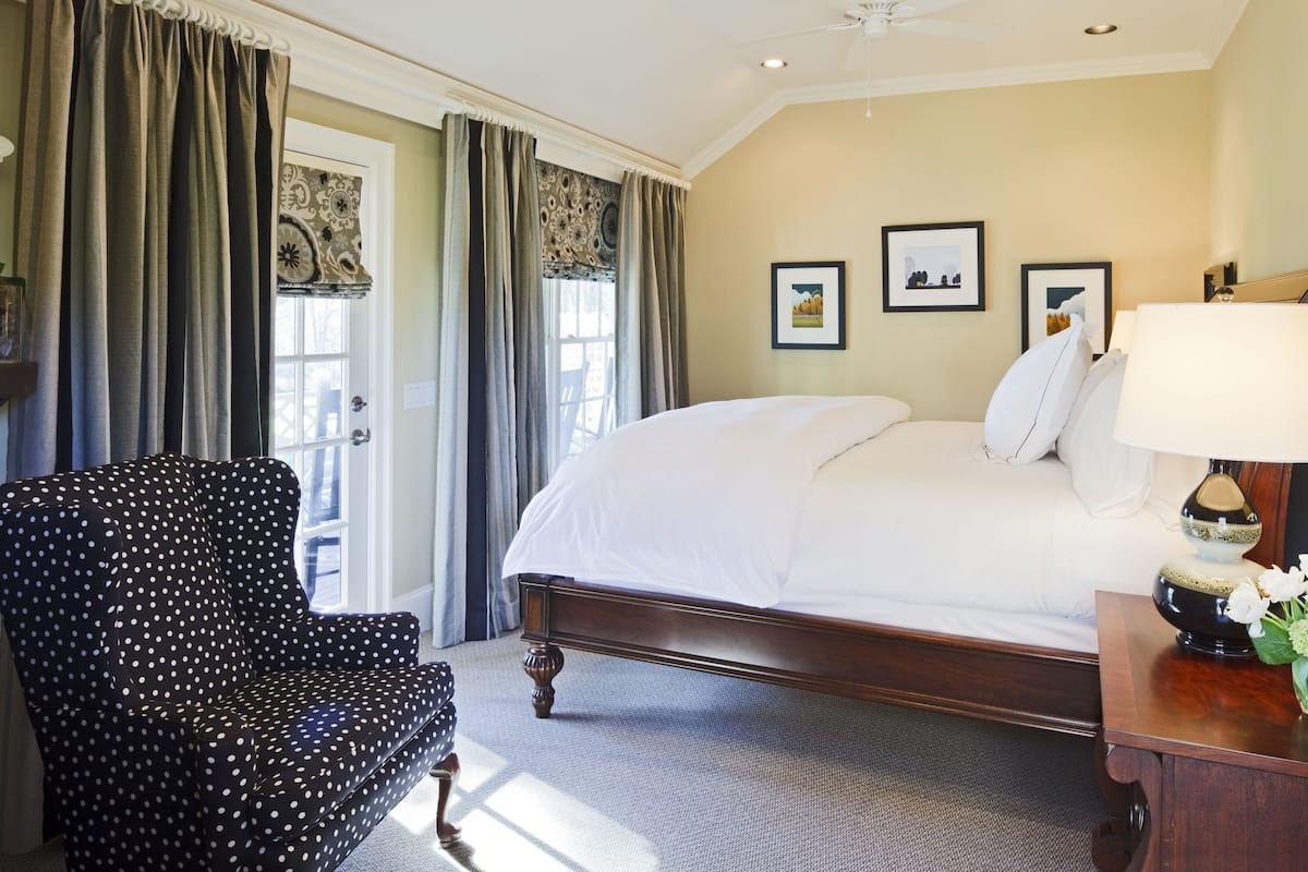 A hotel room with a large bed, a chair, a desk with a lamp, and a vase with flowers.