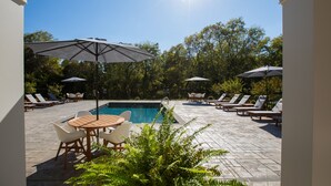 A pool area with lounge chairs and umbrellas, surrounded by trees. - Inn at Willow Grove (Orange)