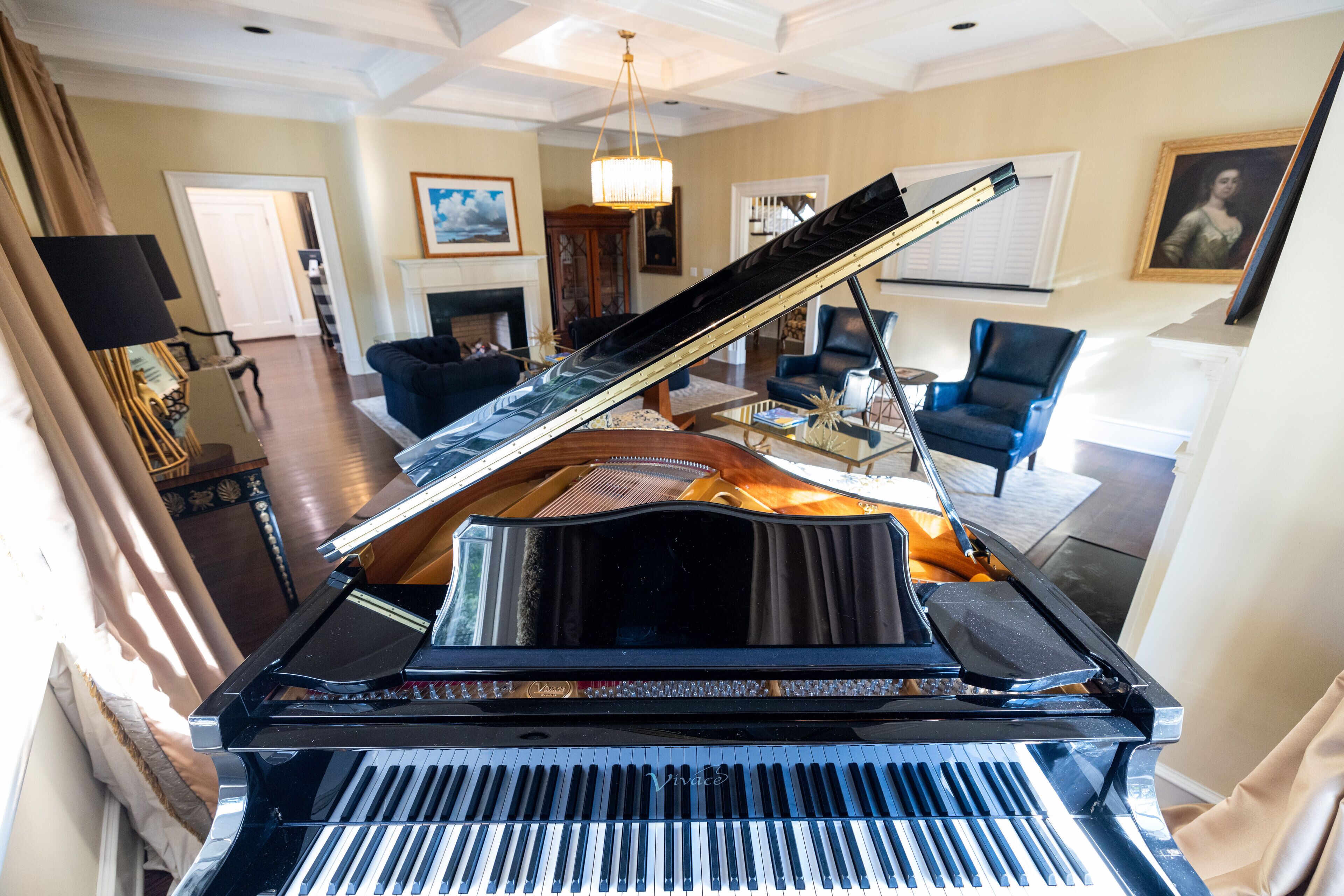 A grand piano in a spacious living room with a high ceiling, a fireplace, and comfortable seating areas.