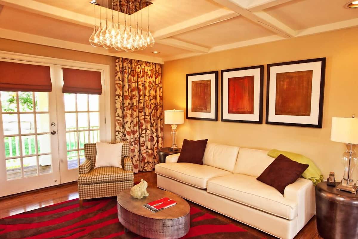 A living room with a sofa, armchair, and coffee table, a chandelier, and three framed artworks on the wall.