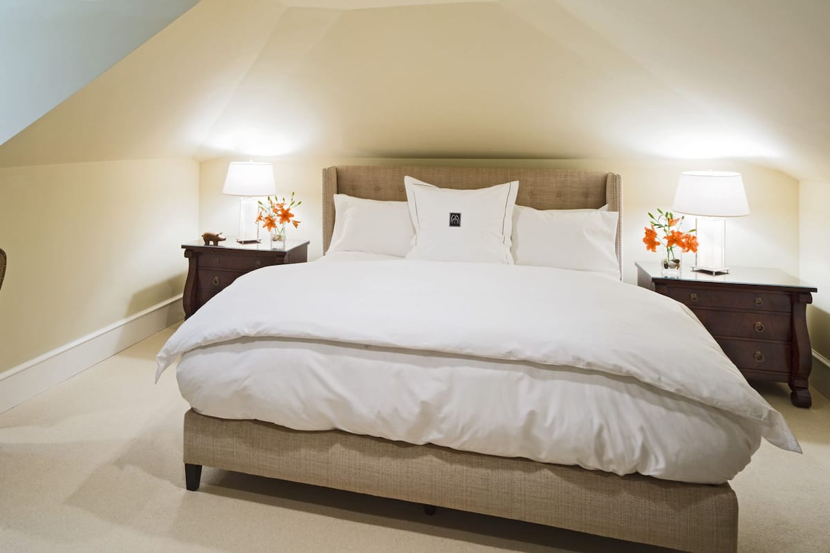 A bedroom with a large bed, two bedside tables with lamps, a chair, and a desk.