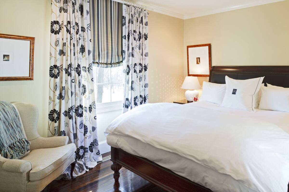A neatly arranged bedroom with a large bed, two bedside tables with lamps, a chair, and floral curtains.