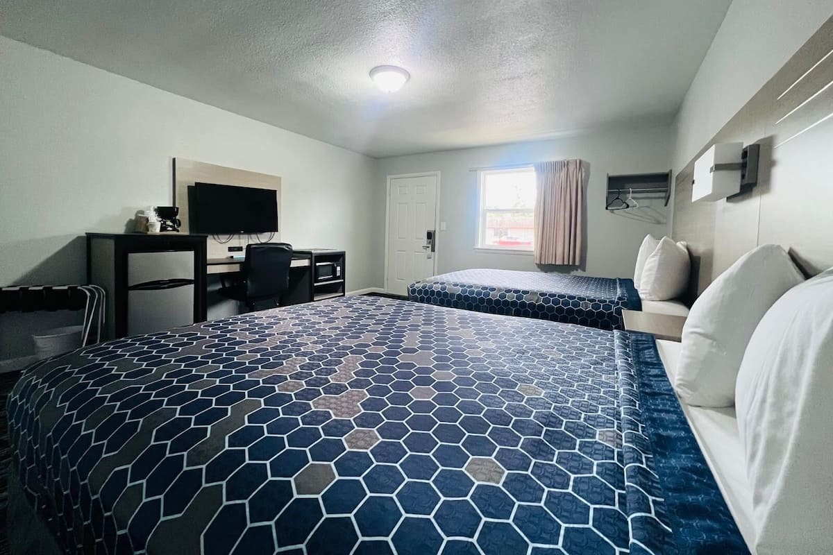 A hotel room with a large bed, a desk with a TV, a chair, and a window with curtains.