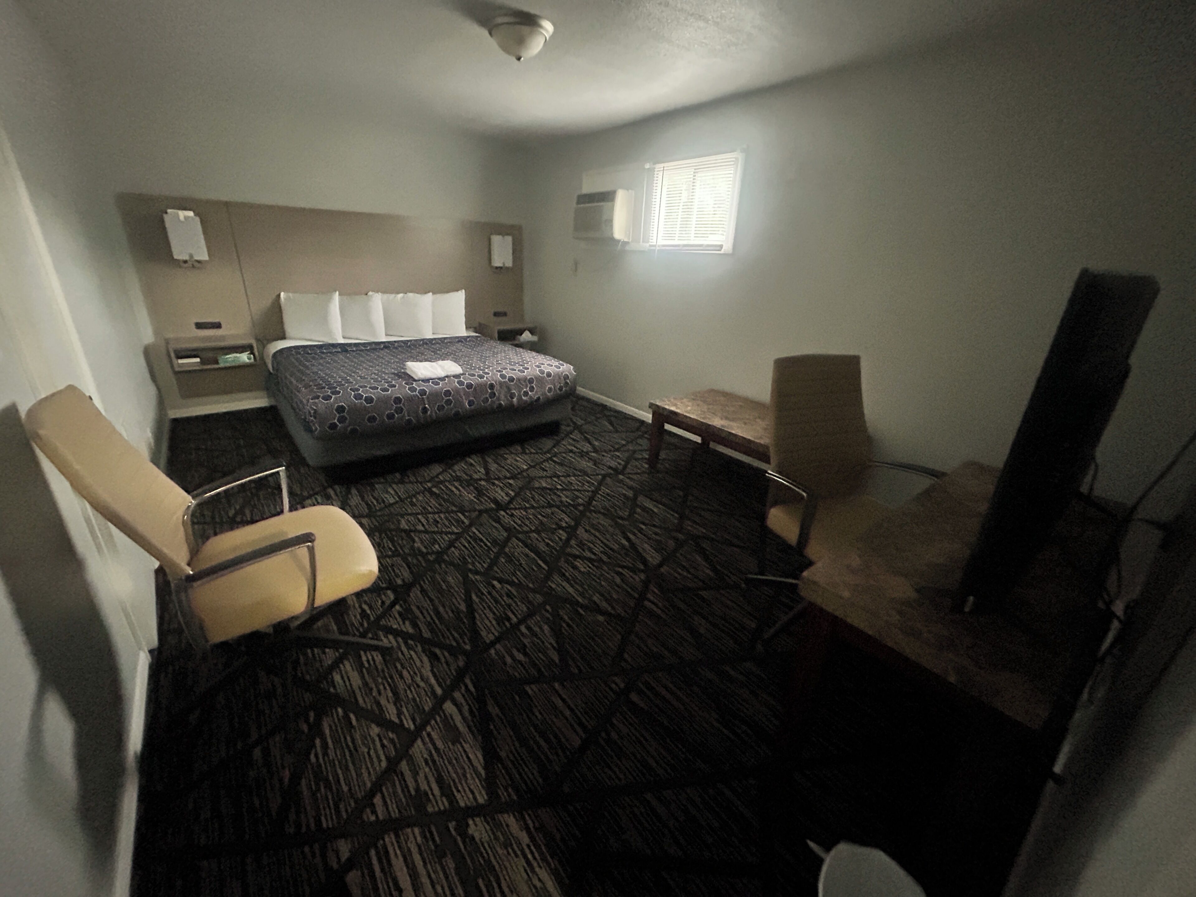 Habitación de hotel con cama, dos sillas, una mesita, televisor y ventana.