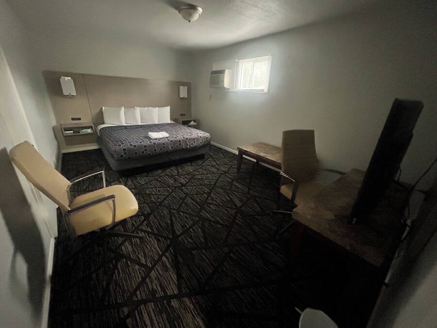 A hotel room with a bed, two chairs, a small table, a TV, and a window.