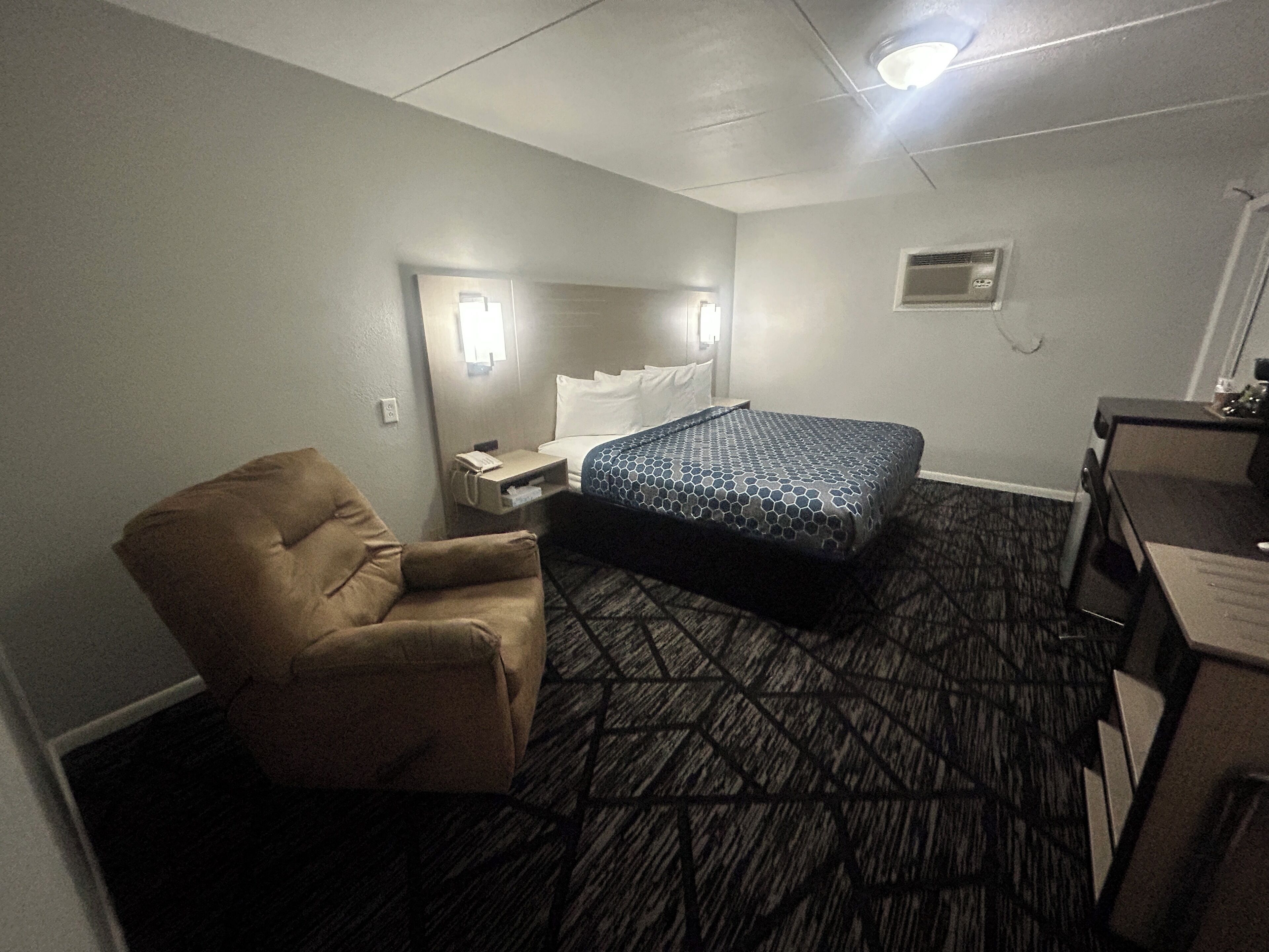 A hotel room with a single bed, a chair, a desk, and a small table.