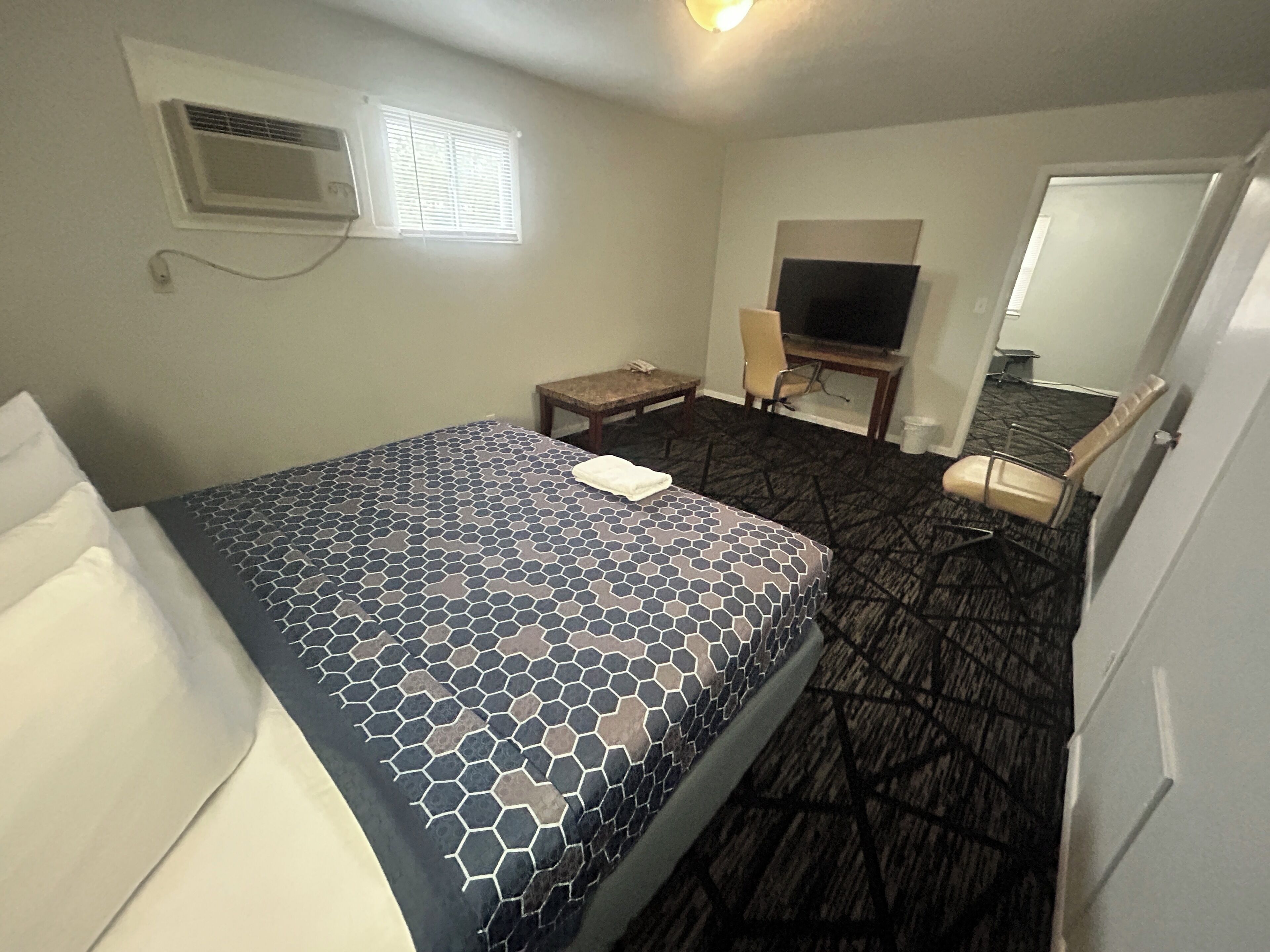 A hotel room with a bed, a desk, a chair, a television, and a mirror.