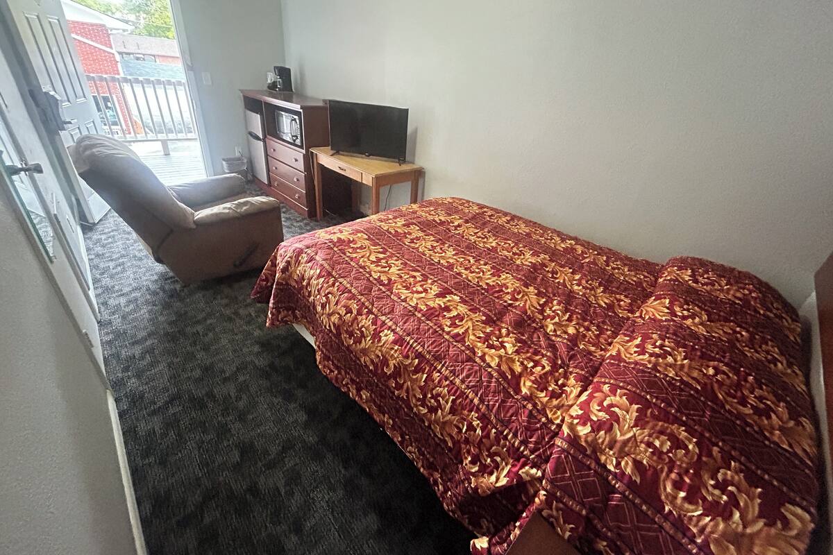 A bedroom with a bed, a chair, a desk, and a TV.