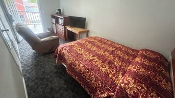Un dormitorio con cama, una silla, un escritorio y un televisor.