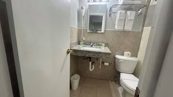Un baño pequeño con lavamanos de granito, un inodoro y un cubo de basura.