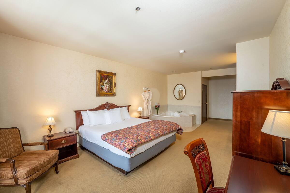 A hotel room with a bed, bedside table, lamp, chair, and a desk with a lamp.