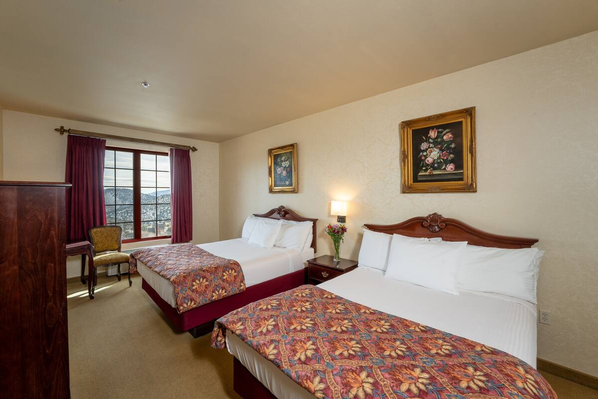 A hotel room with two beds, a desk, a chair, and a window with curtains.