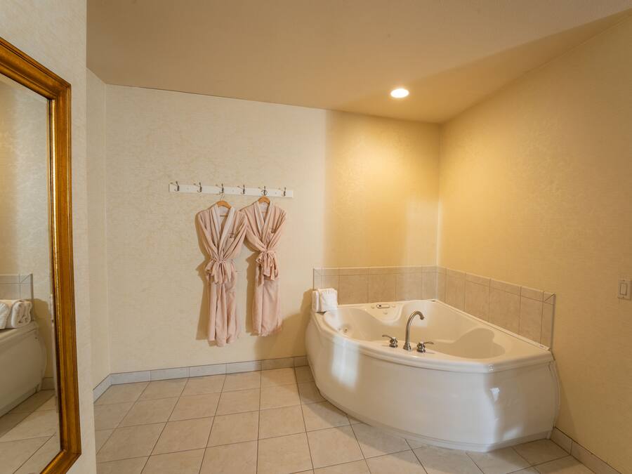 A bathroom with a large bathtub, a towel rack with robes, and a mirror.