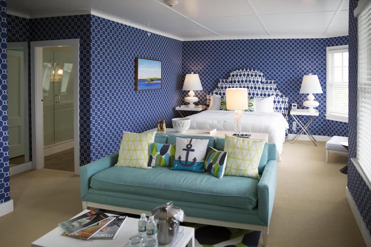 A hotel room with a bed, a teal sofa, and a small table with a magazine and a kettle.