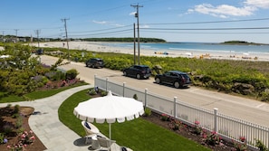 A coastal road with parked cars, a white fence, and a beach in the background. - The Tides Beach Club (Kennebunkport)