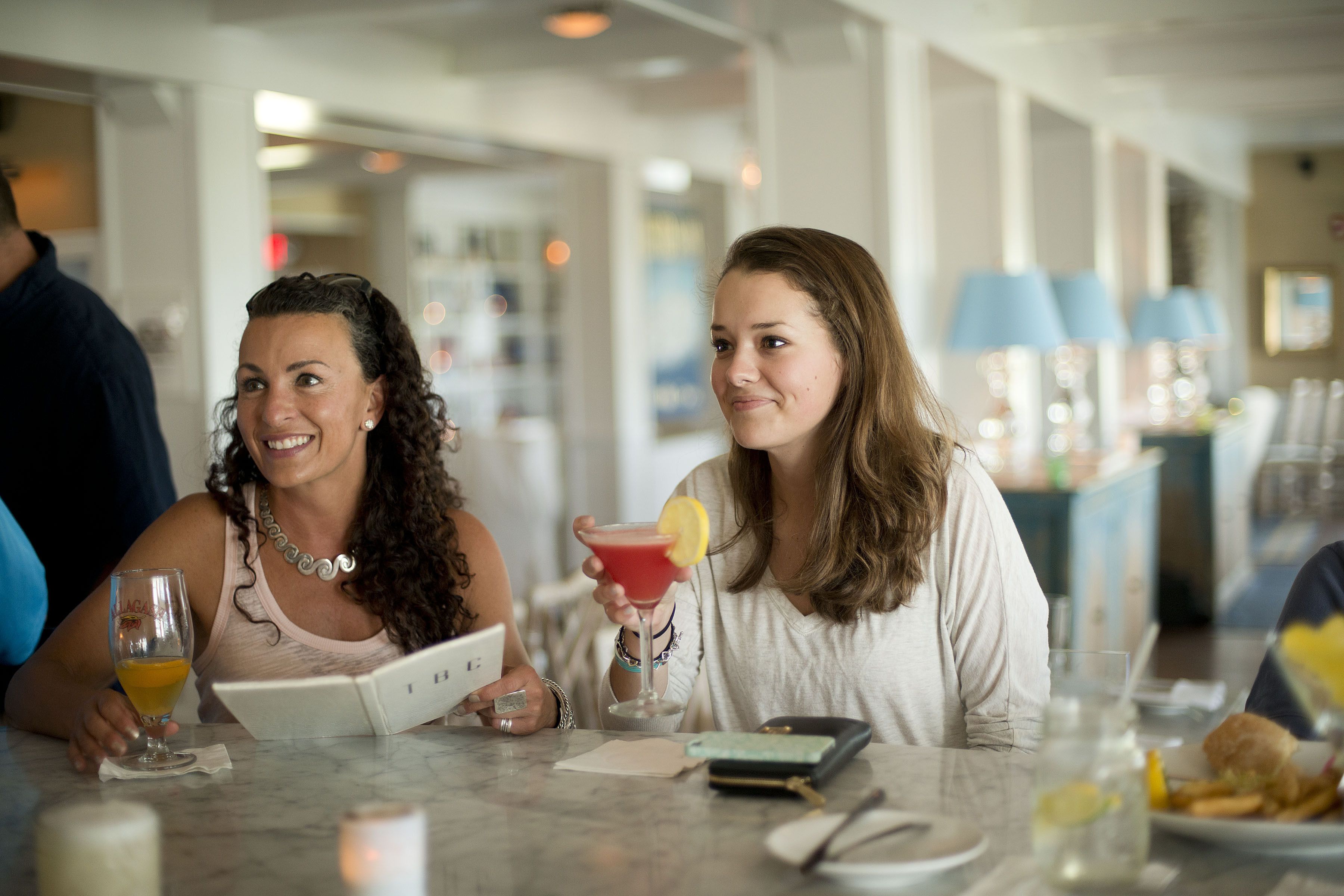 Two people at a table with a menu, a drink with a lemon slice, and a plate with food.