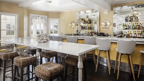 A bar area with a long counter, wicker bar stools, and a variety of liquor bottles. - The Tides Beach Club (Kennebunkport)