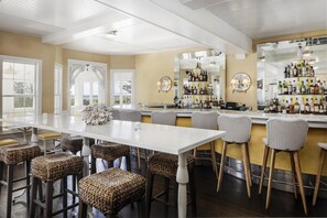 A bar area with a long counter, wicker bar stools, and a variety of liquor bottles. - The Tides Beach Club (Kennebunkport)
