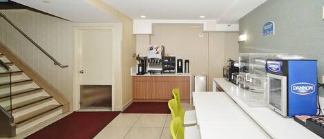 A modern hotel lobby with a staircase, a reception area, and a counter with a coffee machine.
