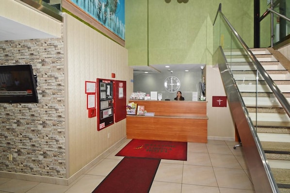 Zona de recepción de un hotel con un escritorio de madera, un reloj y un detector de incendios en la pared.