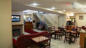 Um saguão de hotel com lareira, escadas e área de refeições com mesas e cadeiras.
