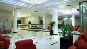 A hotel lobby with a reception desk, red seating, and a large chandelier.