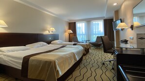 A hotel room with two beds, a desk, a chair, a TV, and a window with curtains.