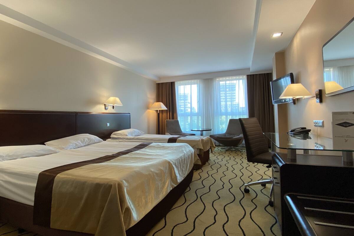 A hotel room with two beds, a desk, a chair, a TV, and a window with curtains.