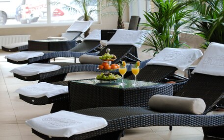 A sun lounge area with wicker furniture, a glass table with fruit and drinks, and a view of the outside.