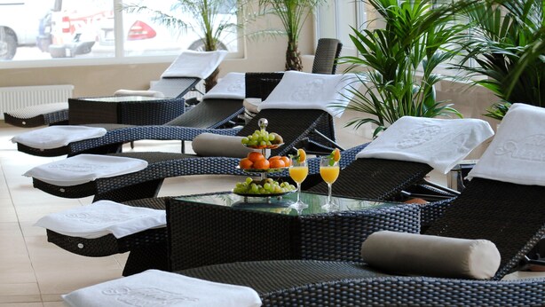 A sun lounge area with wicker furniture, a glass table with fruit and drinks, and a view of the outside.