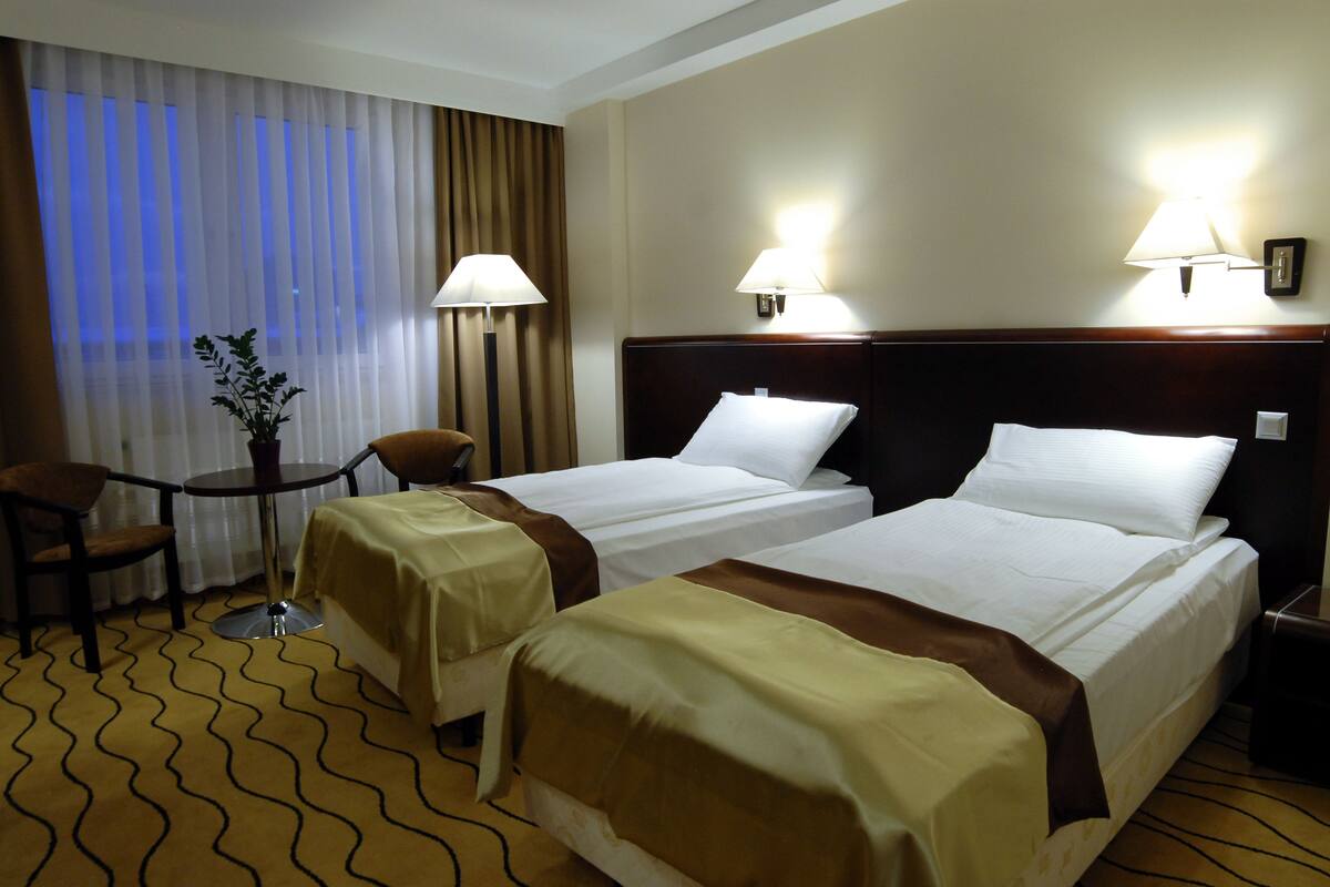 A hotel room with two beds, a chair, a small table, and a potted plant.