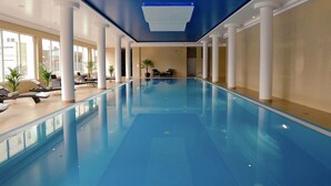 An indoor swimming pool with clear blue water, surrounded by white columns and lounge chairs.