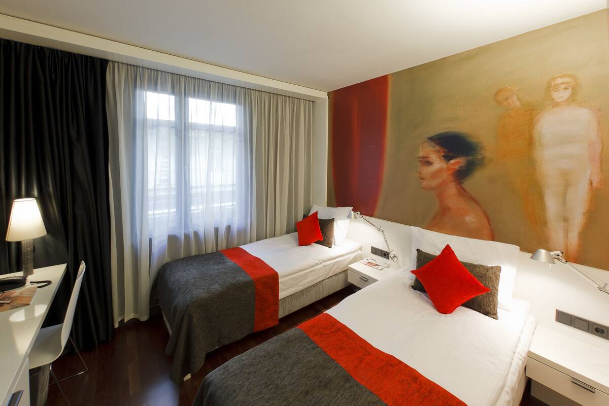 Habitación de hotel con dos camas, un escritorio, una silla, una lámpara y un cuadro en la pared.