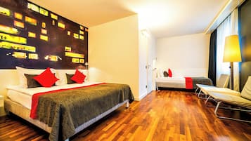 Una habitación de hotel moderna con una cama grande, una cama más pequeña, una zona de estar y un cuadro con una vista urbana.