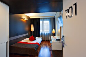 Quarto de hotel com uma cama, uma mesa, uma televisão e a placa com o número 701.