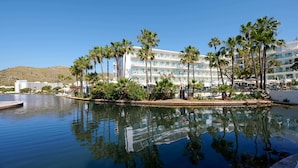 Un hotel con piscina rodeado de palmeras y una montaña al fondo.