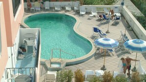 Zona de piscina en la azotea con piscina curva, sillones reclinables y sombrillas.