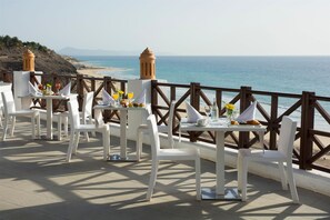 A seaside restaurant with white tables and chairs, a wooden railing, and a view of the ocean. - Club Jandía Princess - All Inclusive (Pajara)
