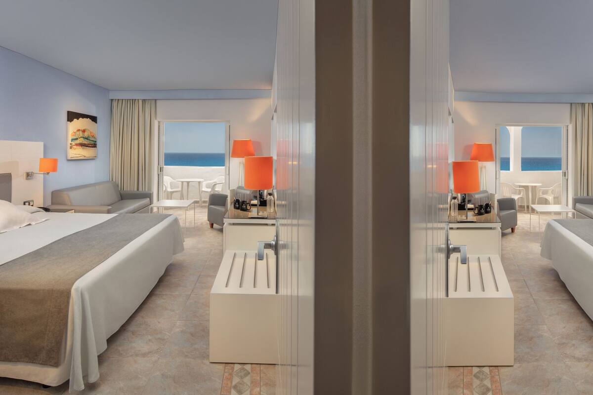 Una habitació d'hotel amb dos llits, un balcó i vista al mar, i un barreter.