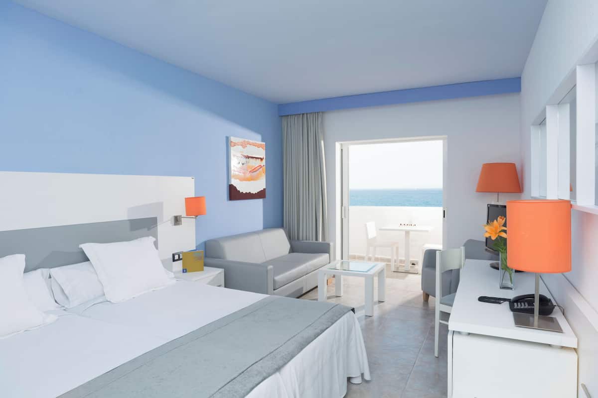 Habitació d'hotel amb llit, sofà, escriptori i vista al mar.