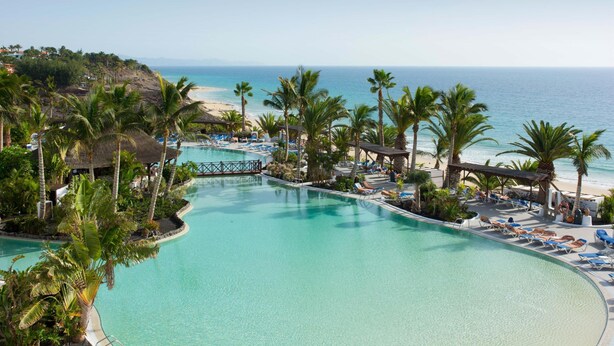 A resort pool area with palm trees, lounge chairs, and a view of the beach. - Club Jandía Princess - All Inclusive (Pajara)