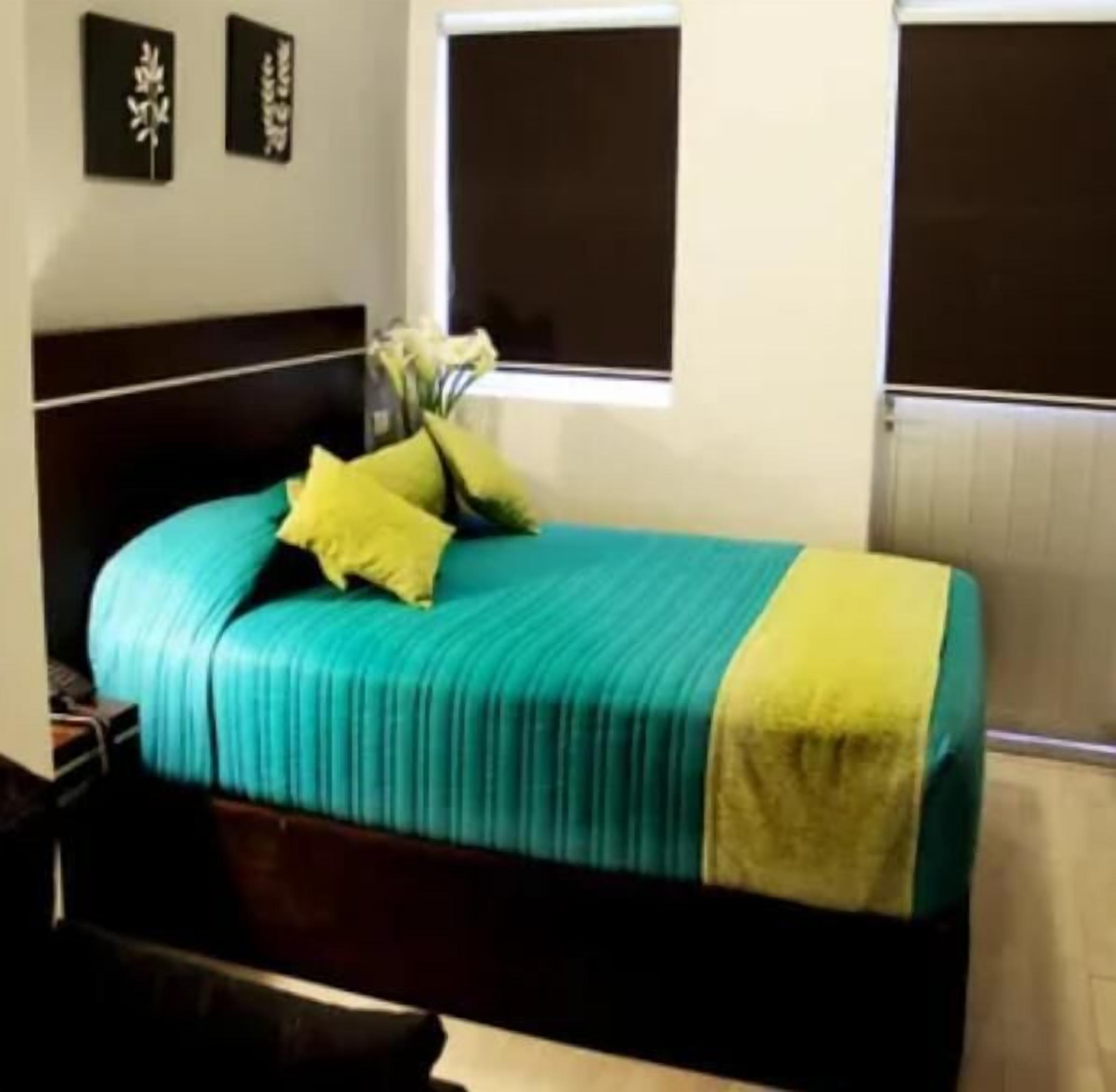 A bed with a teal and yellow bedspread, a wooden headboard, and a nightstand with a lamp.